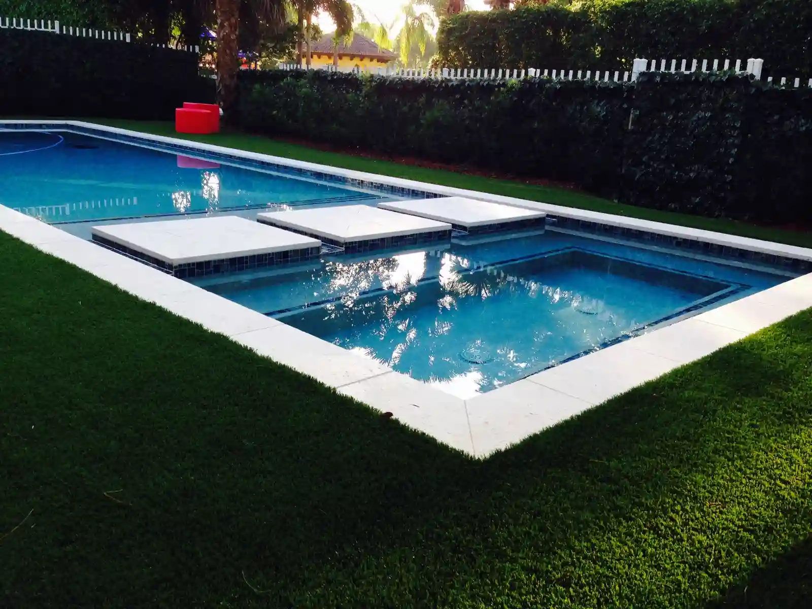 Rectangular pool with a tanning ledge and a safety cover partly across the water on a lawn