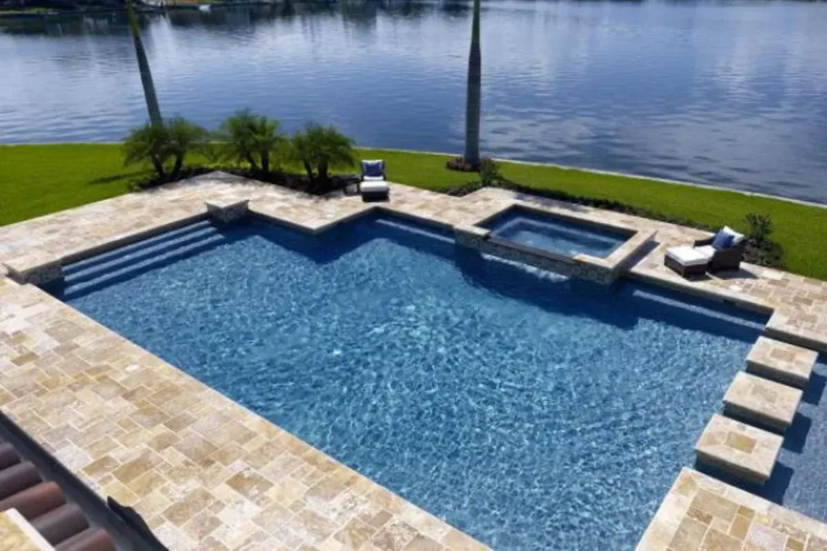 Pool and raised spa with travertine coping on a lakefront lot with a lawn
