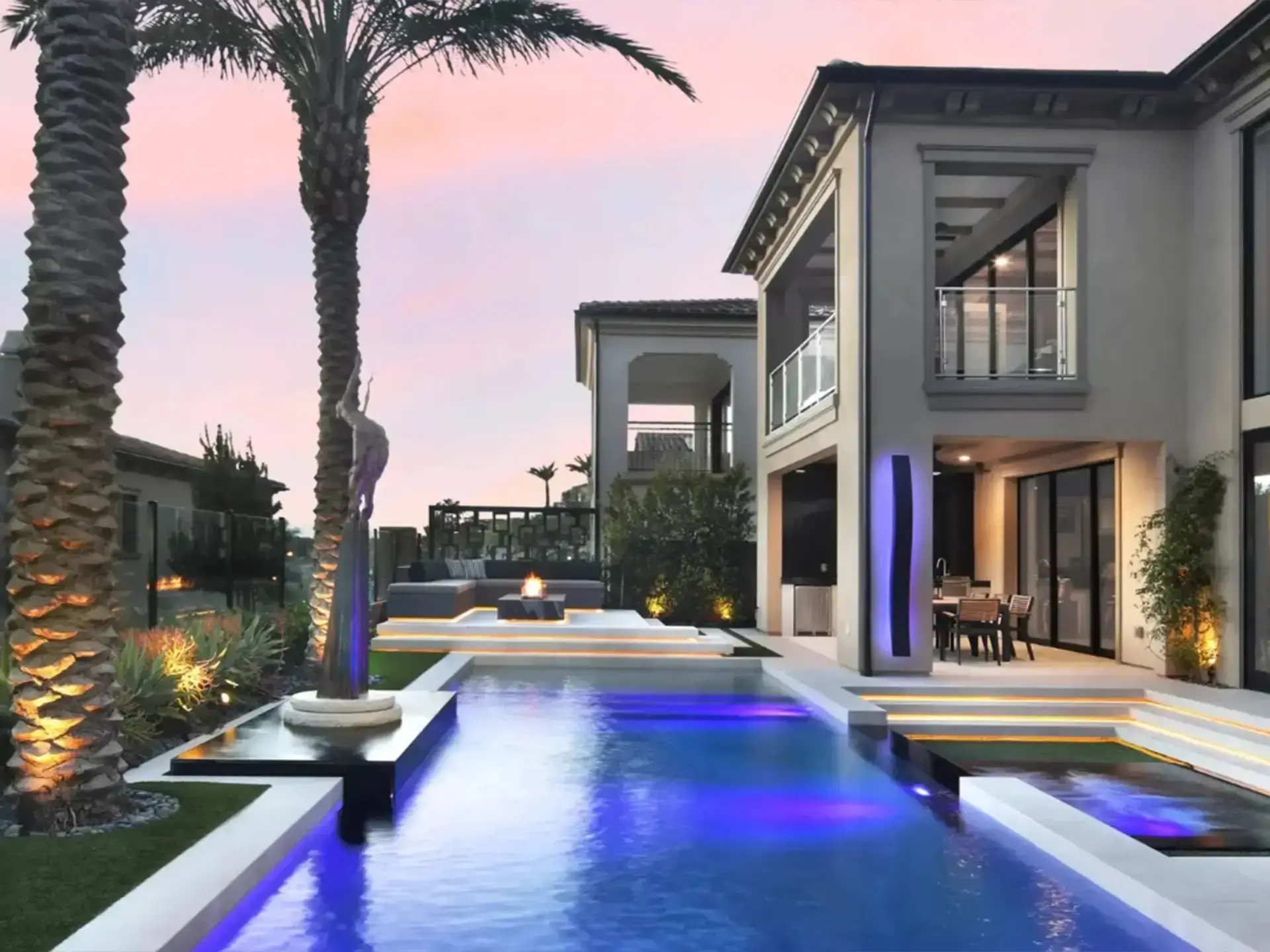 Pool lit purple at dusk with palms and a contemporary home